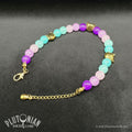 Nothing But the Grin - Alice in Wonderland inspired beaded bracelet. Violet, pink and turquoise glass beads with antique gold-tone grinning cat head beads on a grey velvet background. Plutonian Drift.