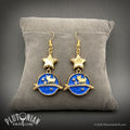 Gold cat astronaut earrings with blue planet charms and star beads displayed on a gray cushion by Plutonian Drift, Celestica, Shop Earrings