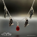Black enamel necklace with four moon-adorned crow charms and a central red teardrop pendant on a silver-tone chain by Plutonian Drift