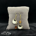Mismatched coffee cat earrings with black cats peeking from white mugs and amber charms on a gray cushion by Plutonian Drift from The Bestiary and Shop Earrings