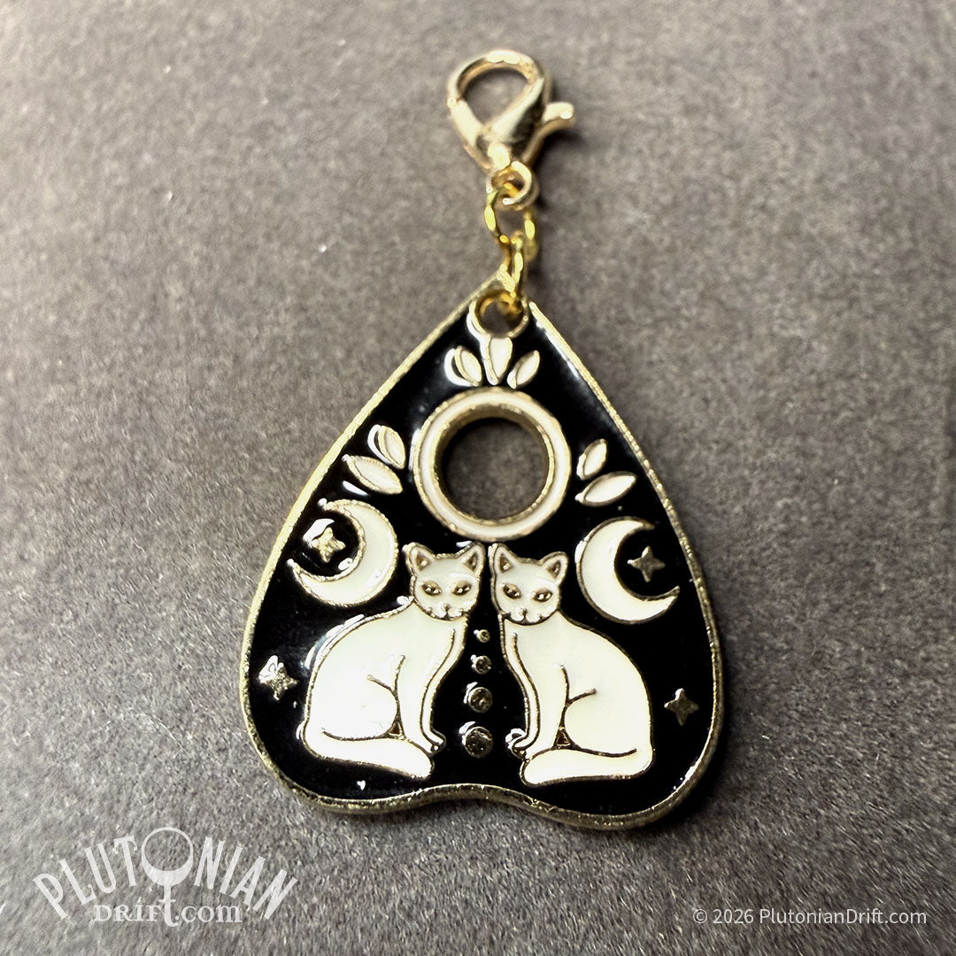 Hello/Goodby ouija necklace. A detachable gold planchette charm with black and white enamel on a grey velvet cloth. Option 4:  two sitting white cats with two crescent moons. Plutonian Drift.